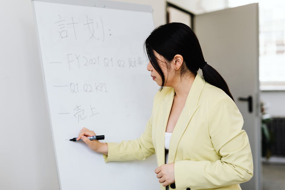 Professional woman in blazer writing on whiteboard during meeting in office setting.